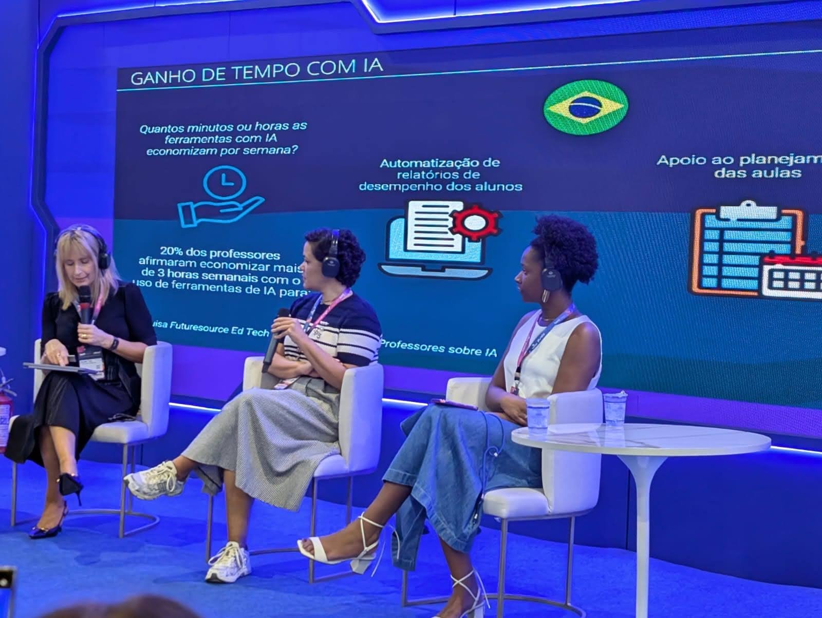 Roberta-Freitas_Empreender-na-educacao_2 Três mulheres sentadas em um palco durante um painel sobre inteligência artificial na educação, com um telão azul ao fundo mostrando dados sobre ganho de tempo com IA para professores, incluindo o dado de que 20% dos professores economizam mais de 3 horas semanais com ferramentas de IA.